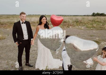 Parents et enfants portant une robe de mariage avec ballons en forme de coeur dans le champ contre le ciel Banque D'Images