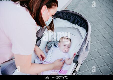 Mère portant un masque de protection, bébé fille endormi dans poussette Banque D'Images