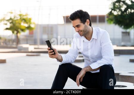 Homme d'affaires charmant utilisant un smartphone assis dans le ciel en ville Banque D'Images