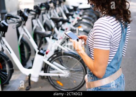 Femme se tenant près de la béquille de stationnement à vélo en utilisant un smartphone ville Banque D'Images