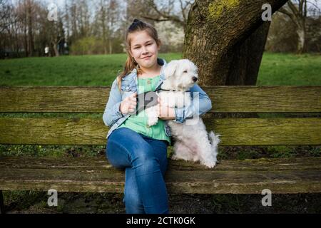 Fille souriante avec un chien assis sur un banc dans le parc Banque D'Images