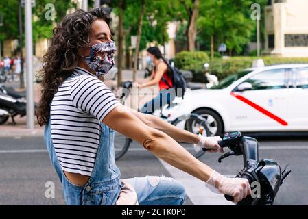 Une heureuse femme à cheval partageant un vélo électrique dans la rue en ville pendant une pandémie Banque D'Images