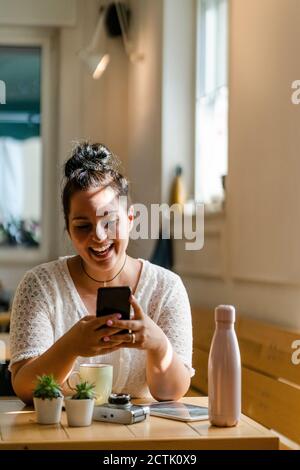 Jeune femme joyeuse utilisant un téléphone portable tout en étant assise à table dans le restaurant Banque D'Images