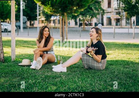 Jeune femme regardant un ami insouciant jouant ukulele pendant qu'elle est assise sur terre herbeuse Banque D'Images