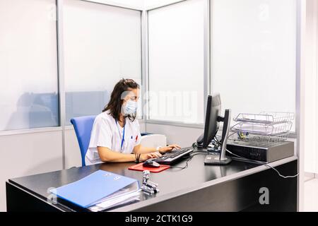 Femme médecin portant un masque chirurgical en utilisant un ordinateur sur le bureau bureau à l'hôpital Banque D'Images