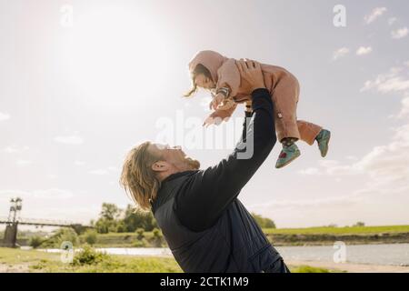 Père levant bébé fille dans l'air près de la rive de la rivière jour ensoleillé Banque D'Images