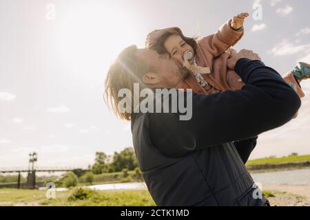 Père embrassant bébé fille sur joue près de la rive de la rivière sur jour ensoleillé Banque D'Images