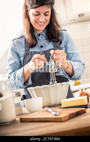 Femme souriante utilisant un tire-paille tout en se tenant dans la cuisine à accueil Banque D'Images