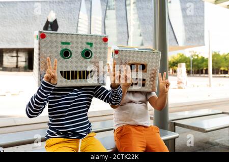 Les garçons portent des masques robotisés montrant le signe de la paix lorsqu'ils sont assis siège à la gare Banque D'Images