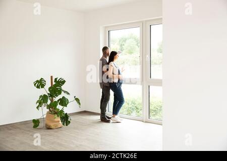 Couple regardant à travers la fenêtre tout en se tenant près de la maison dans la nouvelle maison Banque D'Images