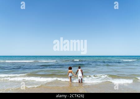 Couple tenant les mains tout en marchant dans la mer contre le ciel clair Banque D'Images