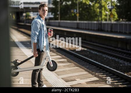 Jeune homme transportant un scooter de poussée en attendant à la gare plate-forme Banque D'Images