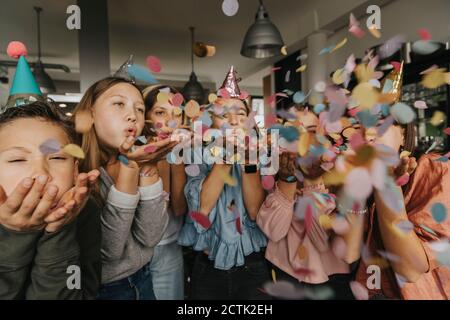 Des amis joueurs soufflent des confettis tout en appréciant la fête d'anniversaire à la maison Banque D'Images