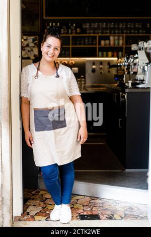 Femme souriante propriétaire debout près de la porte vitrée à l'entrée de café-restaurant Banque D'Images