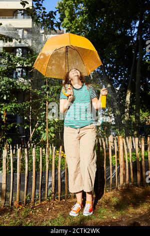 Jeune femme riant avec parapluie et limonade dans le jardin Banque D'Images