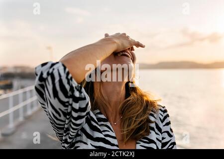 Femme souriante couvrant le visage avec la main contre le ciel clair Banque D'Images