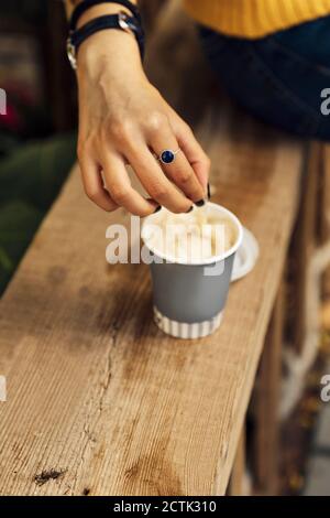 Main de femme remuant le café dans une tasse jetable sur bois banc Banque D'Images