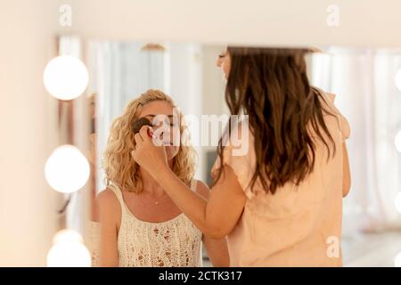 Esthéticienne appliquant le maquillage à une cliente qui réfléchit sur le miroir studio Banque D'Images