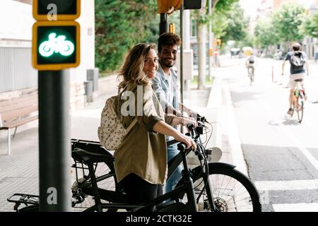 Jeune couple souriant avec des vélos électriques sur le trottoir Banque D'Images