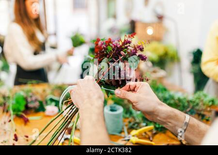 Fleuriste nouant main le bouquet de fleurs avec l'équipe qui travaille arrière-plan à la boutique de fleurs Banque D'Images