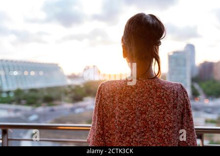 Femme debout sur le balcon tout en regardant le coucher du soleil Banque D'Images