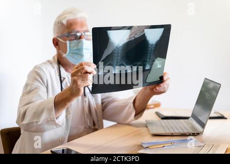 Médecin examinant les rayons X médicaux du cou humain tout en étant assis clinique Banque D'Images