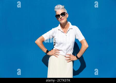 Femme âgée debout avec la main sur la hanche contre le mur bleu par beau temps Banque D'Images