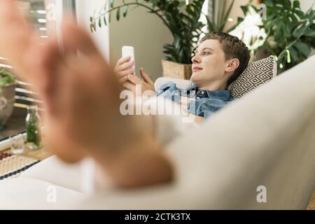 Femme de taille moyenne avec un smartphone reposant sur un canapé dans la salle de séjour Banque D'Images