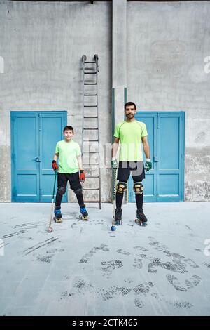 Homme et fils matures tenant des bâtons de hockey contre les portes à cour Banque D'Images