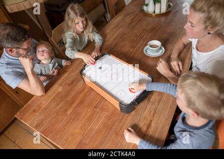 Les enfants jouent au hockey pneumatique à la table de salle à manger avec leurs parents pendant week-end Banque D'Images