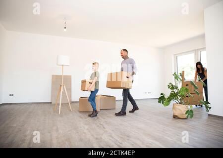 Père et fils transportant des boîtes en carton tout en marchant sur du bois dur étage dans une nouvelle maison Banque D'Images