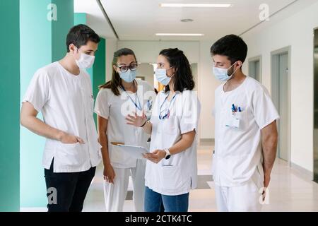 Les médecins portant des masques chirurgicaux discutant au-dessus d'une tablette numérique debout à l'hôpital Banque D'Images