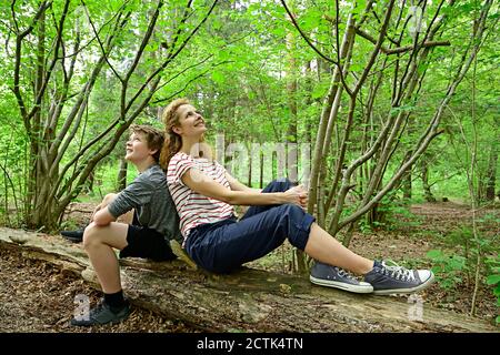 Mère et fils attentionnés, assis dos à dos sur les morts arbre en forêt Banque D'Images