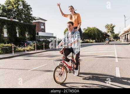 Jeune femme gaie debout derrière un petit ami à vélo dans la rue Banque D'Images
