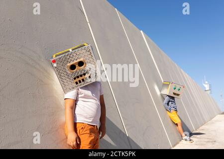 Garçons portant des masques robotisés contre le mur en ville jour ensoleillé Banque D'Images