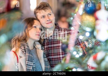 Jeune couple aimant regardant l'arbre de Noël et les lumières dedans ville Banque D'Images