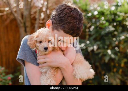 Jeune garçon embrassant le chiot dans la cour arrière Banque D'Images