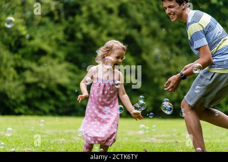 Un frère joyeux jouant avec sa sœur au milieu de bulles dans le parc public Banque D'Images