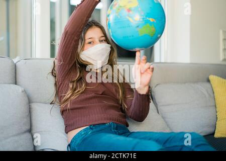 Une fille avec un globe portant un masque facial tout en étant assise sur un canapé à la maison Banque D'Images