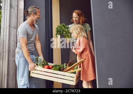 Femme souriante tenant des légumes tandis que le père et la fille portant la caisse à l'entrée Banque D'Images