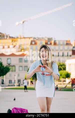 Jeune femme gaie en forme de coeur tout en étant debout en ville Banque D'Images