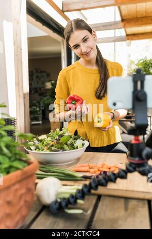 Femme souriante filmant avec un téléphone portable tout en préparant des repas à accueil Banque D'Images