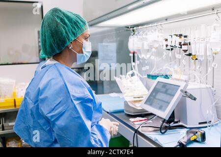 Femme scientifique qui regarde les gouttes d'iv accrochées sur le support à l'intérieur laboratoire Banque D'Images