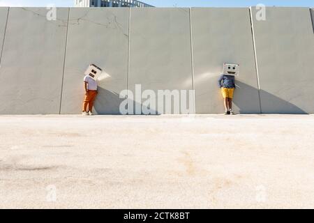 Amis portant des masques robotisés debout contre le mur en ville jour ensoleillé Banque D'Images