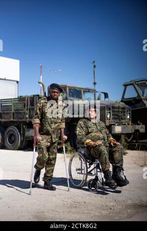 Officier militaire blessé tenant des béquilles en se tenant debout avec une armée handicapée soldat en fauteuil roulant pendant la journée ensoleillée Banque D'Images