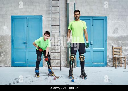 Homme mature et son fils tenant des bâtons de hockey contre les portes au tribunal Banque D'Images