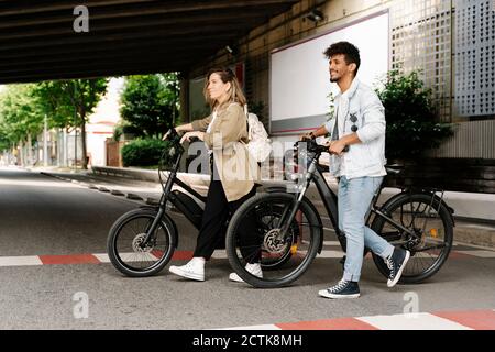 Couple traversant la route avec des vélos électriques dans la ville Banque D'Images