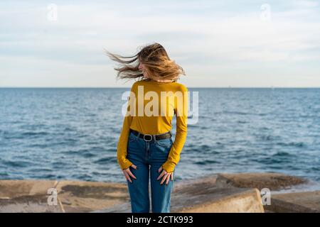 Une femme souriante se lance sur les cheveux tout en appréciant contre la mer Banque D'Images