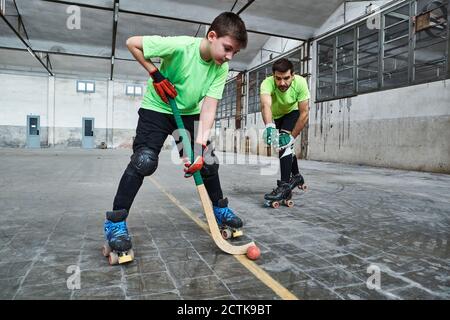 Garçon pratiquant le hockey sur rouleaux avec son père sur le terrain Banque D'Images