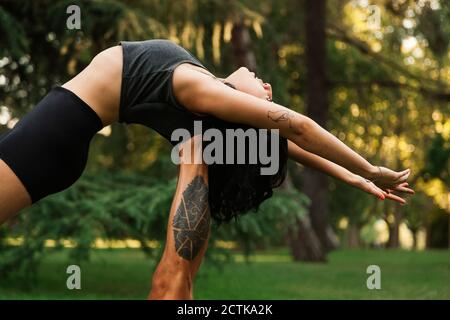 Petit ami levant petite amie sur les jambes tout en pratiquant acroyoga dans le parc Banque D'Images